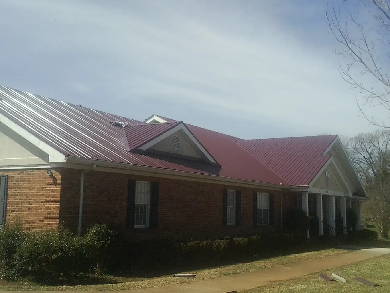 Red metal roof with gabled entries on a long brick building, from a Hail Damage Roof Repair job in Schenevus