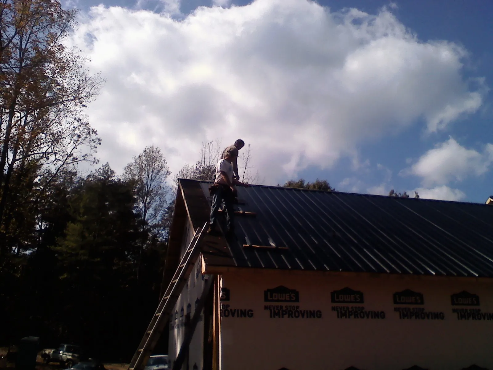 Roofer fastening dark metal panels high against a cloudy sky, from a Roof Inspection job in Schenevus