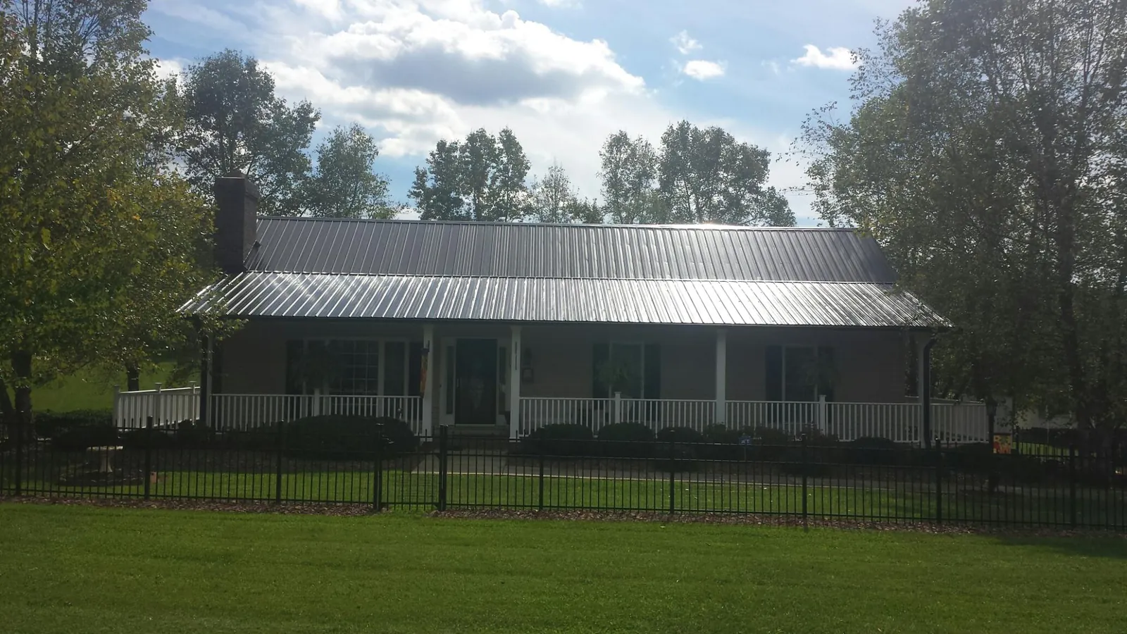 Gray metal roof on a brick ranch with a full width front porch — Gutter Guard Installation work by our crew in Schenevus